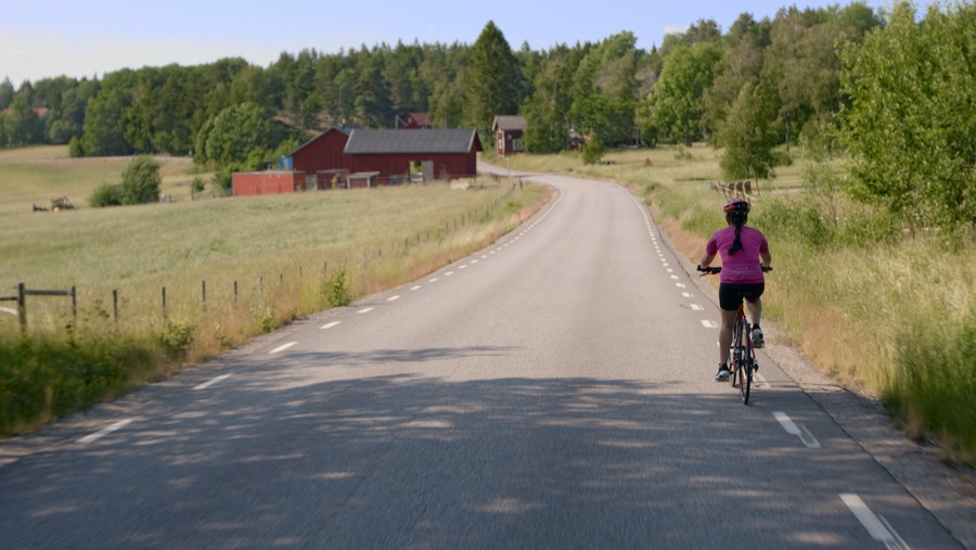 Kvinna som cyklar längs landsväg på sommaren
