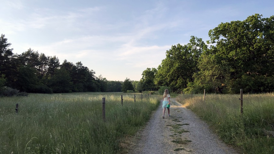 Flicka går längs grusväg en vacker sommarkväll. 